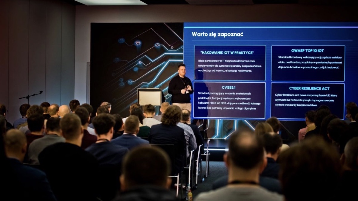 Jakub Lipiec na scenie INSECON przed pełną salą, na ekranie slajd o standardach bezpieczeństwa IoT